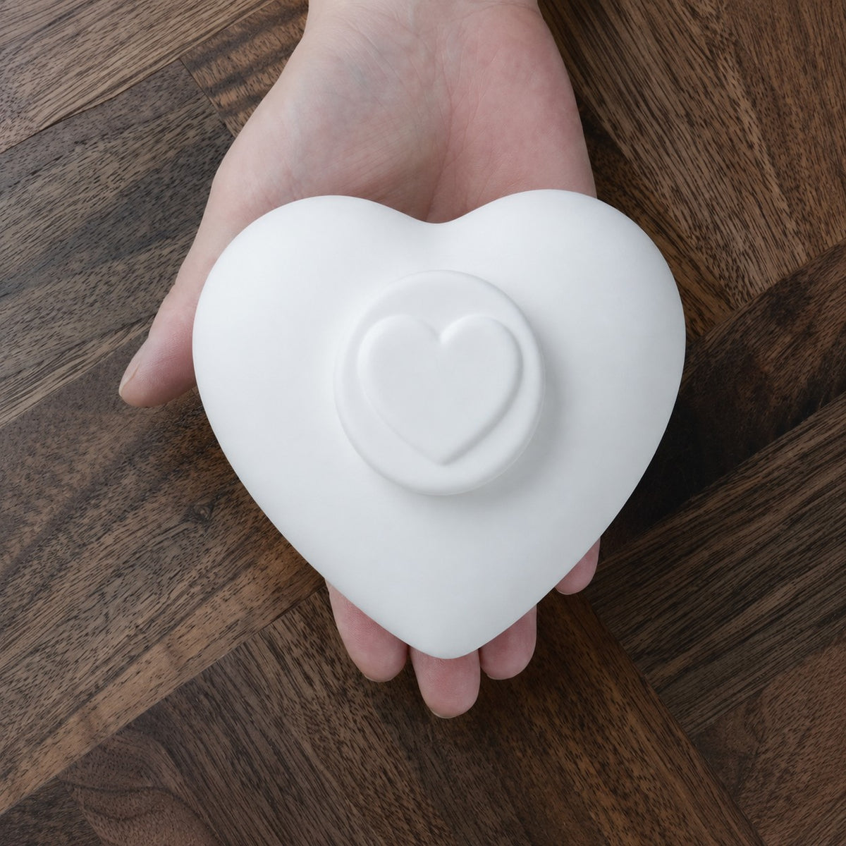 Hartvormige urn voor kat of hond in mat wit keramiek in een handpalm