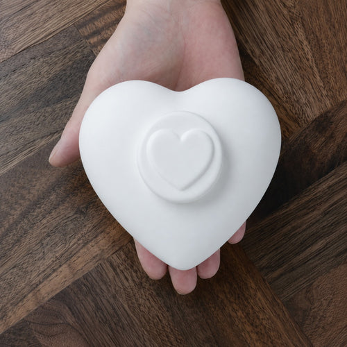 Hartvormige urn voor kat of hond in mat wit keramiek in een handpalm