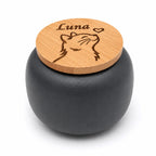 De laatste aai mini-urn van zwart keramiek met een gegraveerde bamboe deksel met kattenafbeelding en naam.