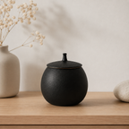 Matzwarte keramische mini urn voor hond of kat op een houten plank