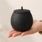 Ronde matzwarte mini urn van keramiek in een hand