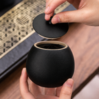 Zwarte keramische mini urn met deksel, vastgehouden in handen