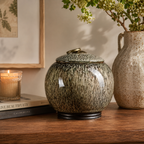 De laatste aai ronde keramische urn met glanzende natuurlijke textuur, geplaatst op een houten dressoir.