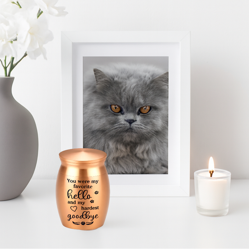 De laatste aai roségouden RVS mini-urn met inscriptie voor as van huisdieren naast een fotolijst en kaars