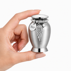 De laatste aai mini urn van RVS met gepersonaliseerd naamplaatje en decoratieve bedeltjes in een hand vastgehouden.