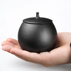 De laatste aai keramische mini-urn voor honden in zwart met deksel, vastgehouden in een handpalm.